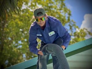 Technician on a roof handling a flexible hose during a smoke test inspection for plumbing or ventilation systems