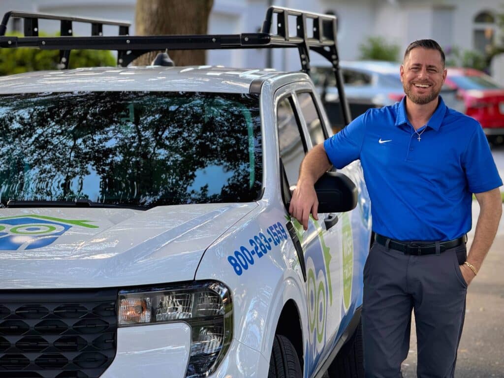 Dennis Man in a blue polo leaning against a white pest control truck with company branding