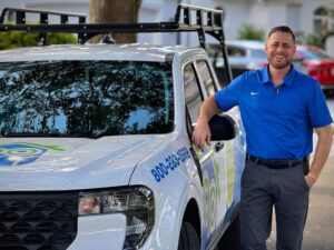 Dennis Man in a blue polo leaning against a white pest control truck with company branding