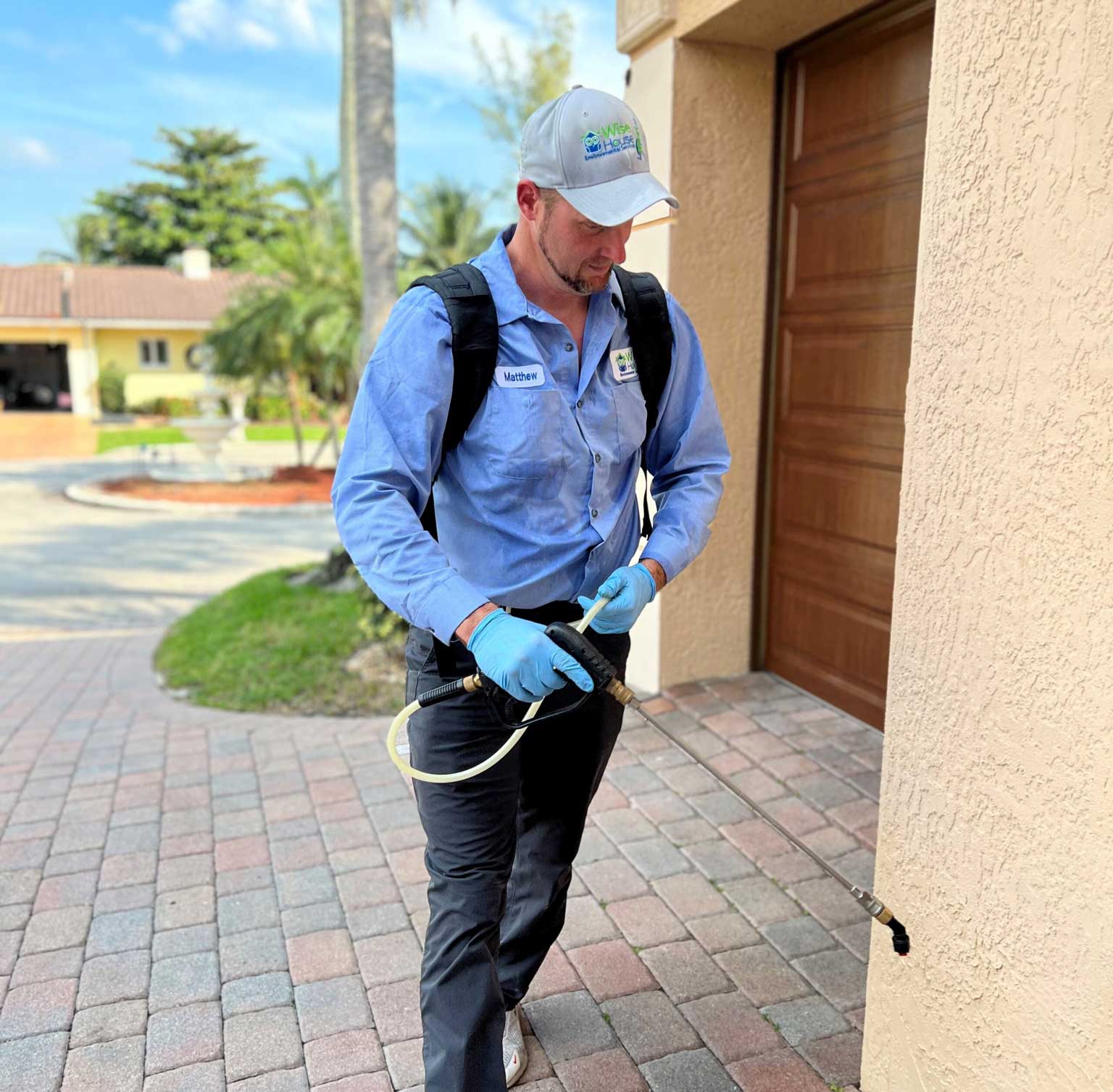 Wise House Pest Control technician treating the exterior of a South Florida home with a backpack sprayer