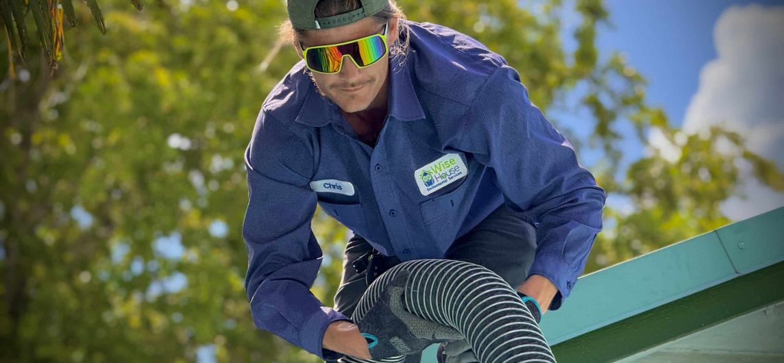 Technician on a roof handling a flexible hose during a smoke test inspection for plumbing or ventilation systems